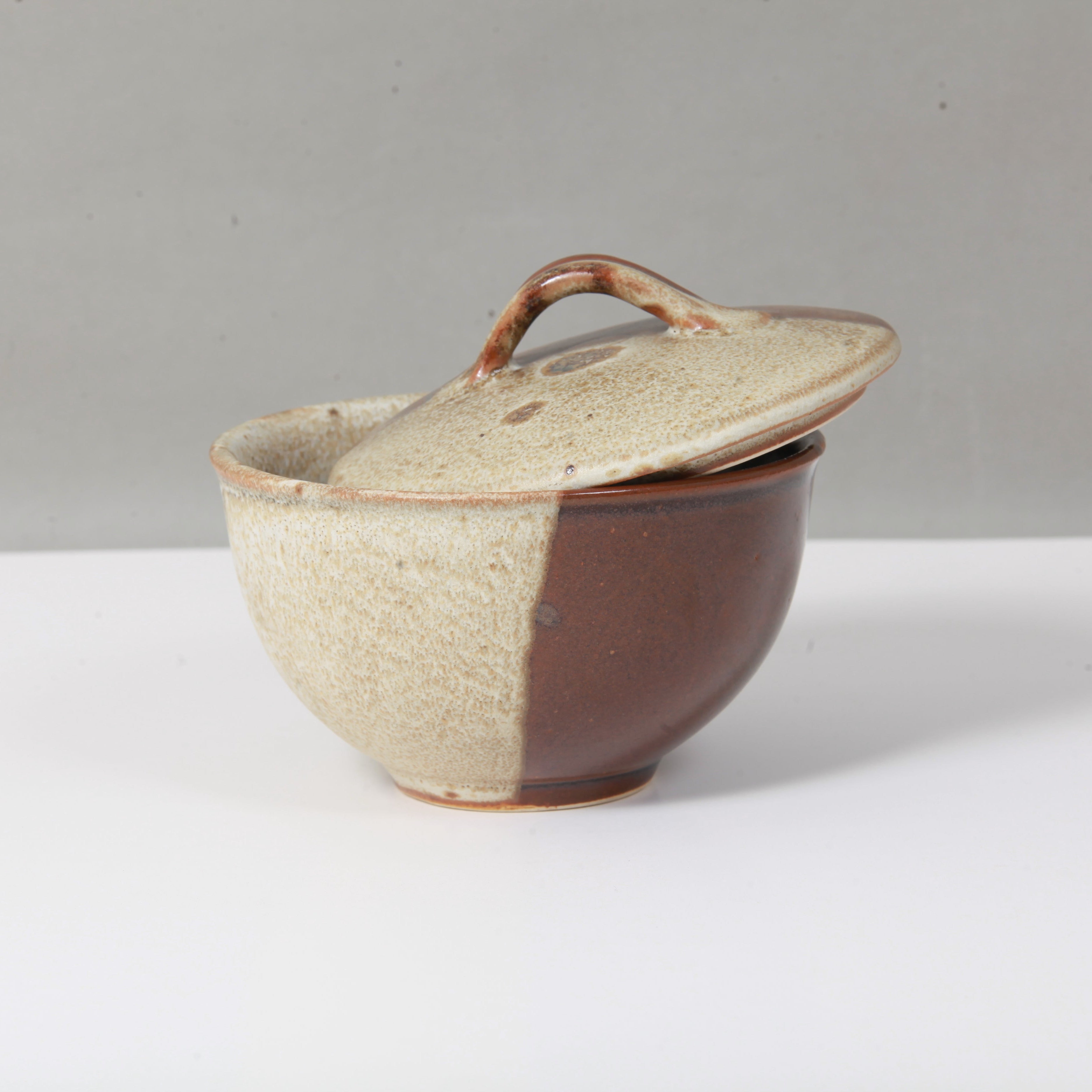 Ceramic pot with a lid on a white surface with a gray background